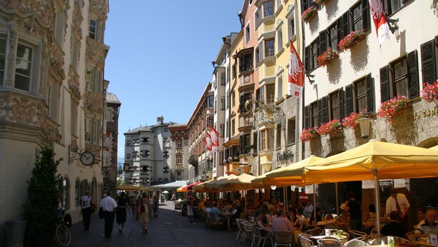 Une rue pavée bordée de cafés, de terrasses et de bâtiments ornés de balcons.