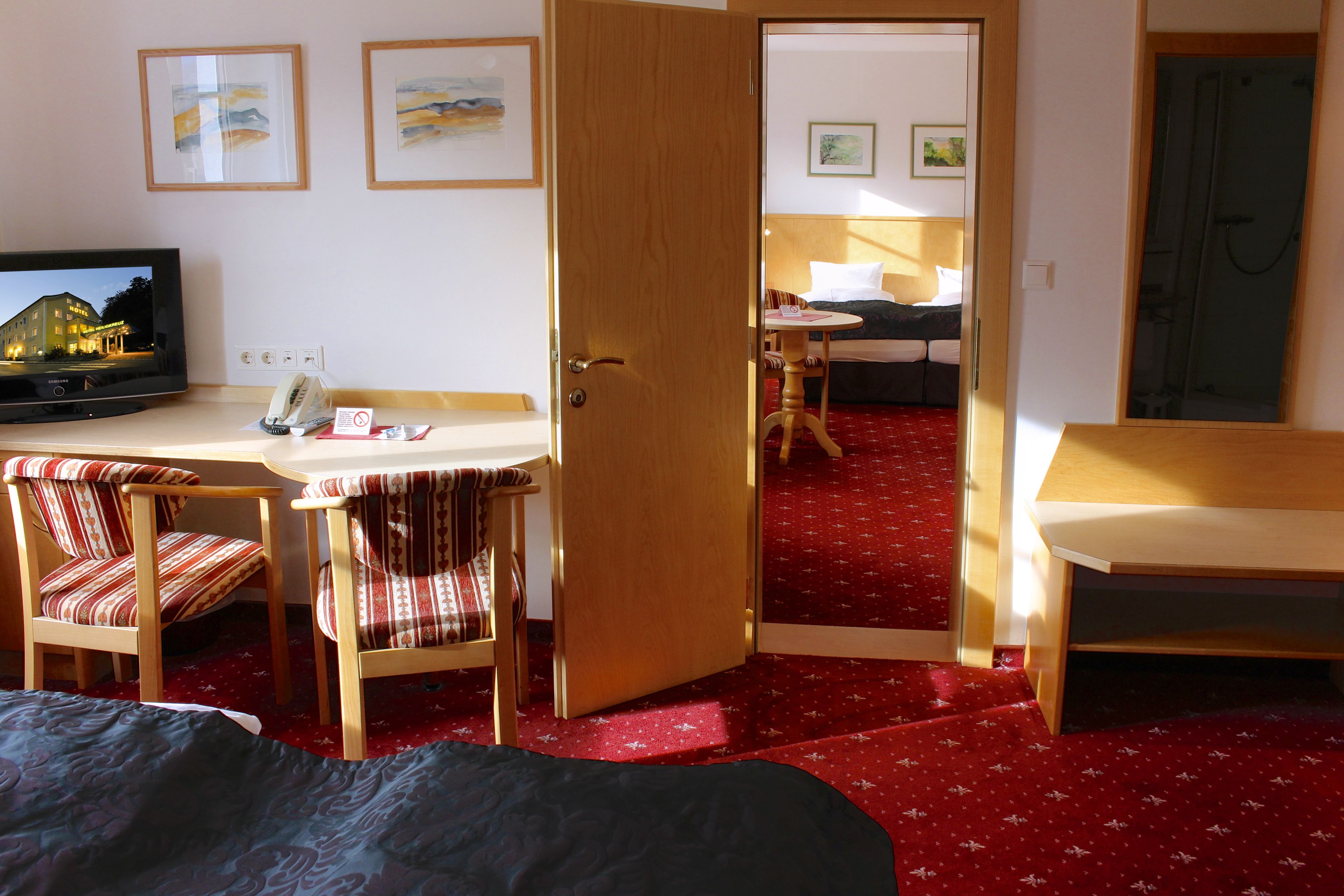 A hotel room with a bed, a desk with a chair, a television, and a door leading to another room.