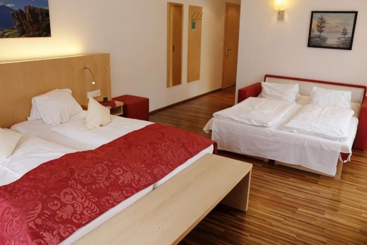 A hotel room with two beds, a wooden floor, a bench, and a painting on the wall.
