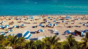 A beach with umbrellas, people, and boats. - The Betsy - South Beach (Miami Beach)