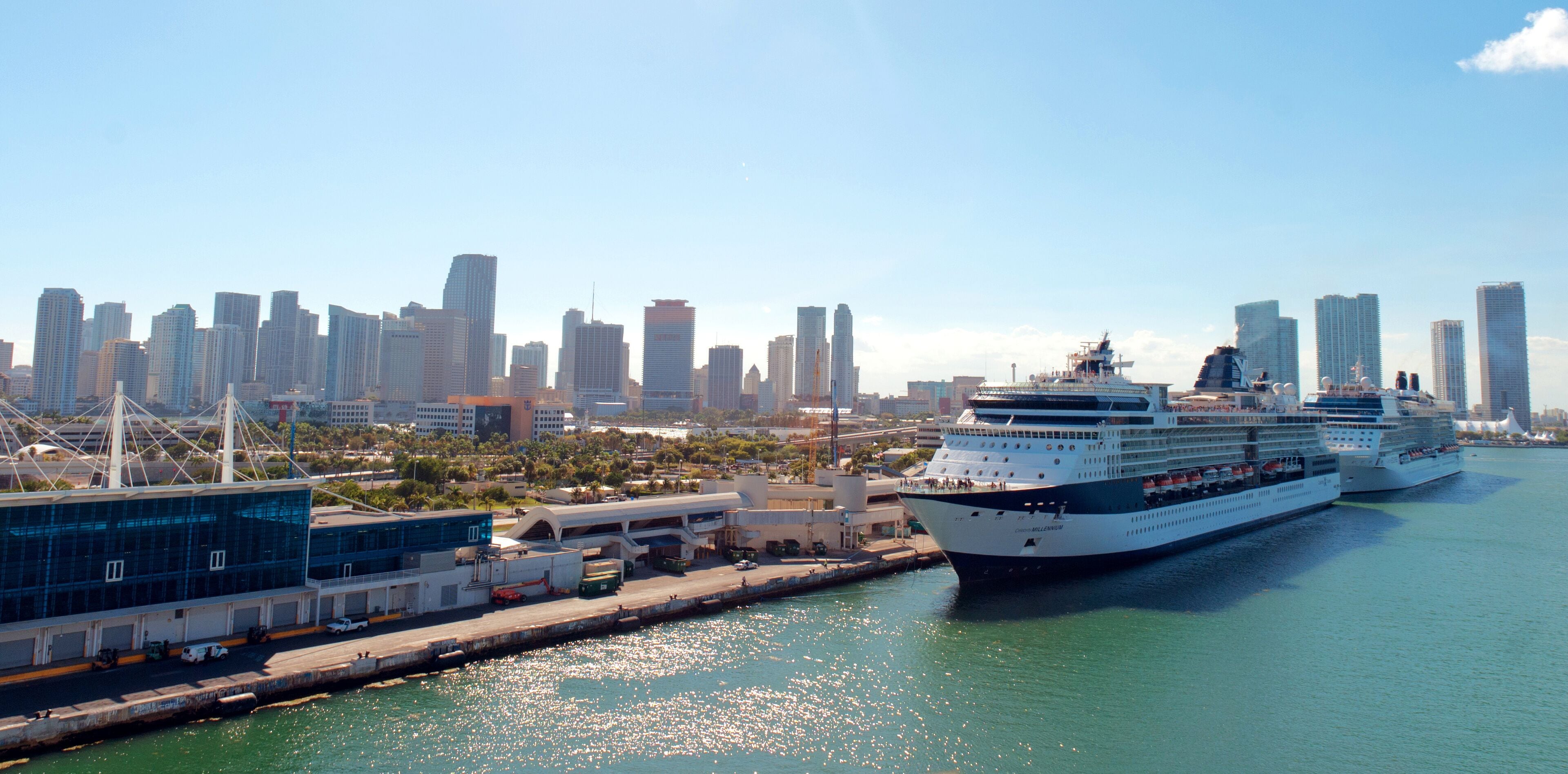 A cruise ship docked at a port with a city skyline in the background.