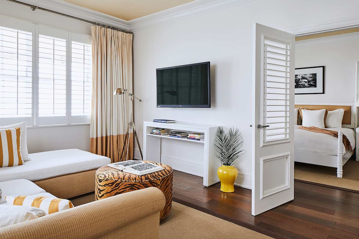Ein Hotelzimmer mit Bett, Sofa, Fernseher, Schreibtisch und einem Fenster mit Vorhängen.