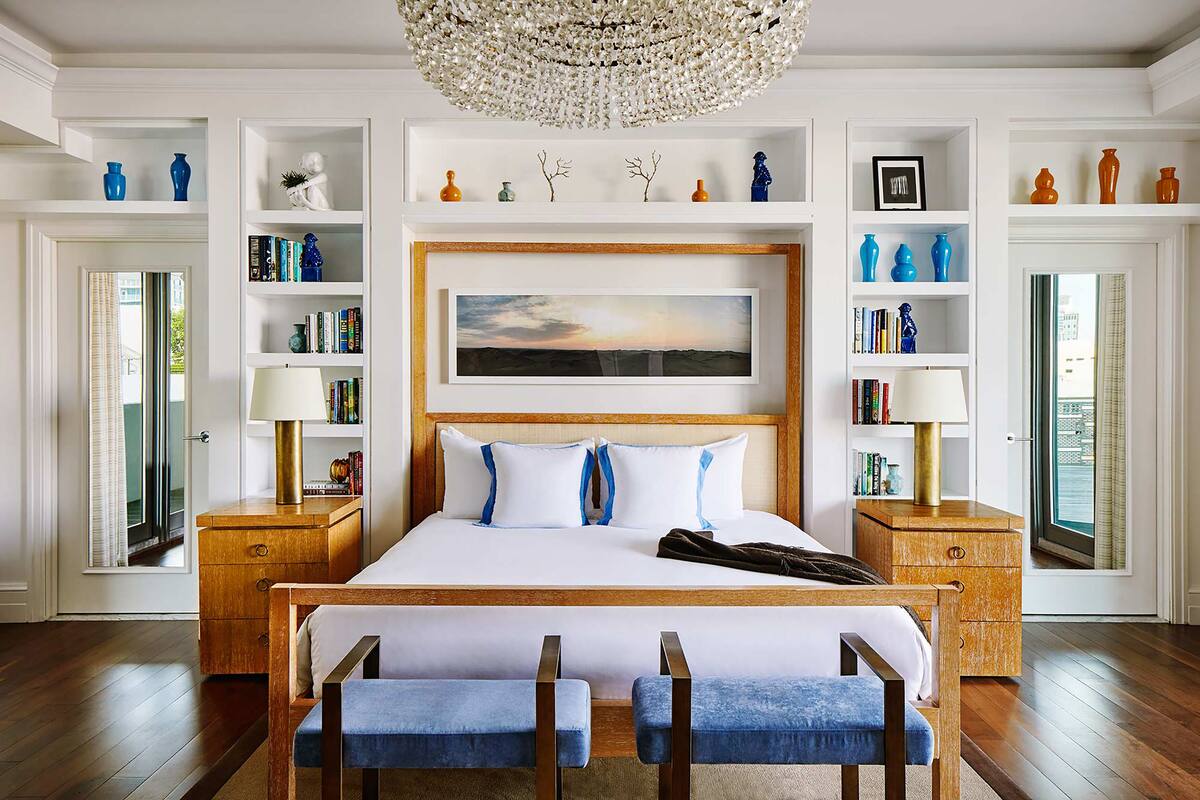 Ein Schlafzimmer mit einem großen Bett, Holzbeistelltischen, einer Chandelierleuchte und eingebauten Regalen mit Büchern und Dekoration.