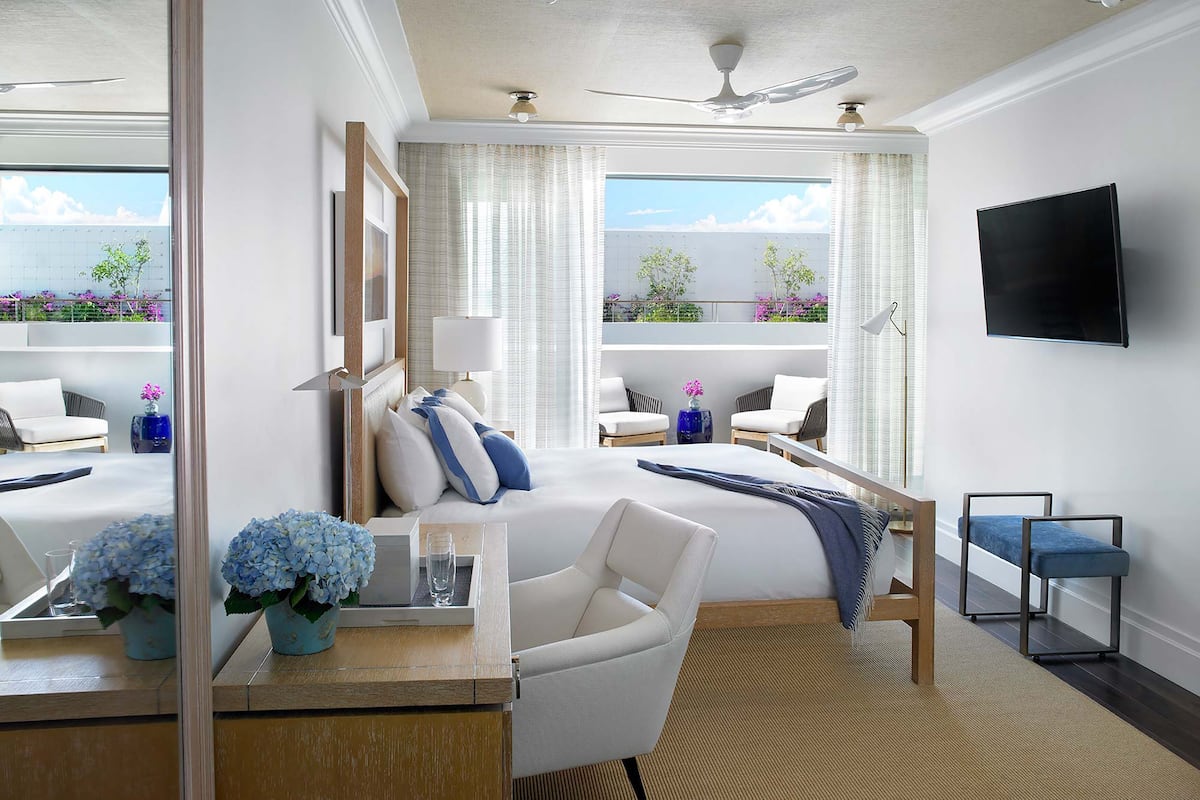 Ein Hotelzimmer mit Bett, Schreibtisch mit Lampe, Stuhl, Fernseher und Blick ins Freie.