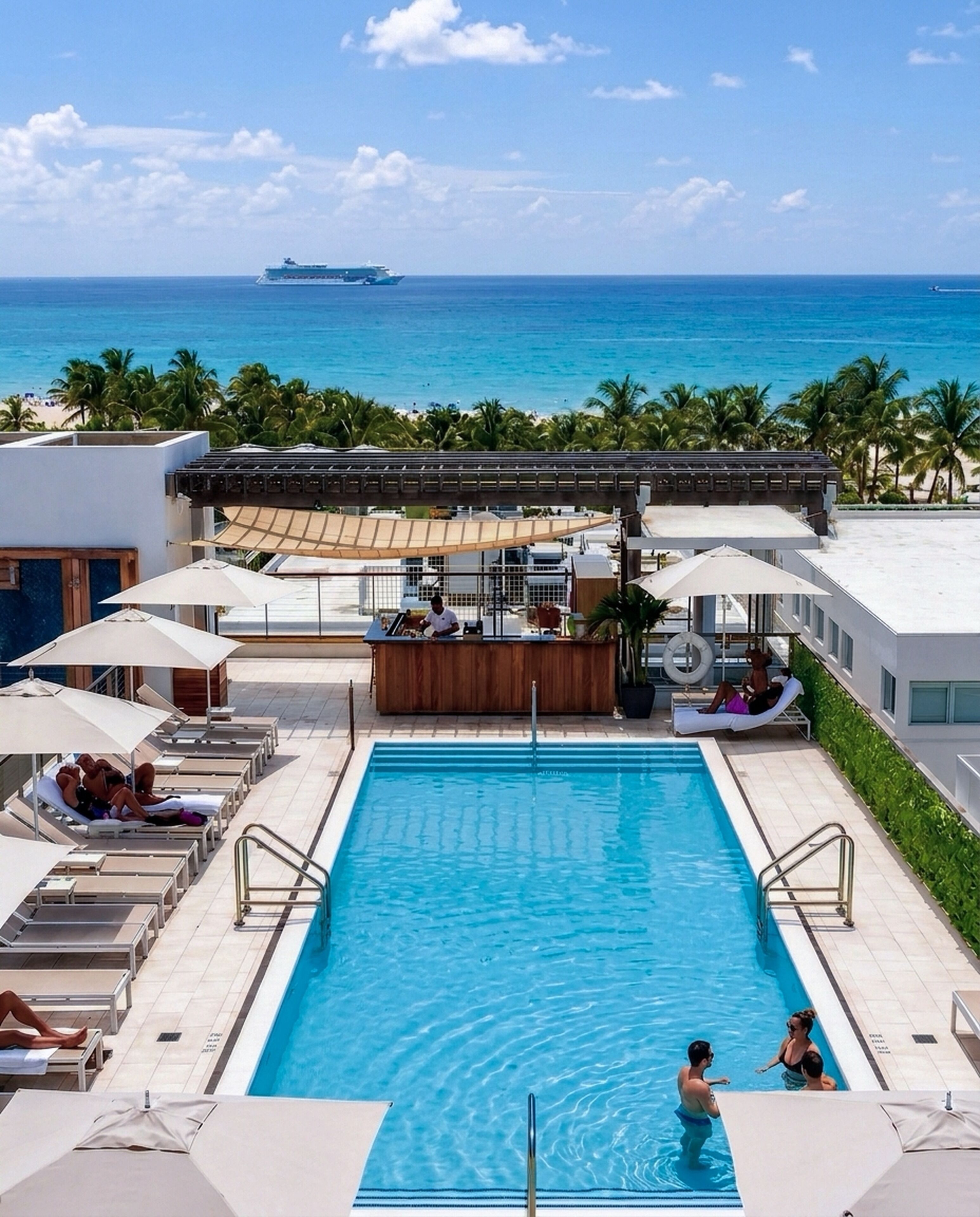 A pool area with lounge chairs, a bar, and a view of the ocean.