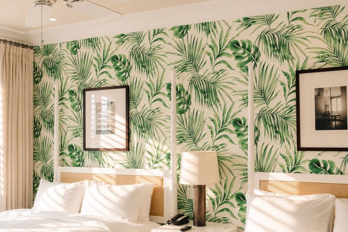 Ein Hotelzimmer mit tropischem Blattmuster-Tapete, einem Bett mit weißer Bettwäsche, einem Nachttisch mit Lampe und einem gerahmten Bild an der Wand.