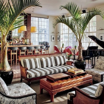 A modern hotel room with a large bed, two blue armchairs, a desk, and a view of the city through large windows. at The Betsy - South Beach