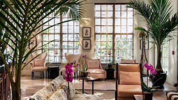 A spacious living room with a ceiling fan, large windows, and various seating arrangements including a patterned sofa and armchairs.