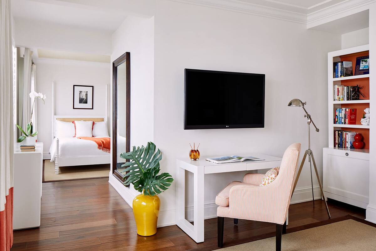 Ein modernes Schlafzimmer mit Bett, Schreibtisch, Stuhl, Fernseher, Bücherregal und einem Blumentopf.