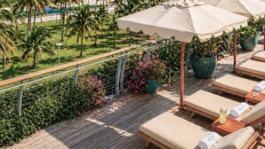 A deck with lounge chairs and umbrellas overlooking a beach with palm trees and the ocean. - The Betsy - South Beach (Miami Beach)