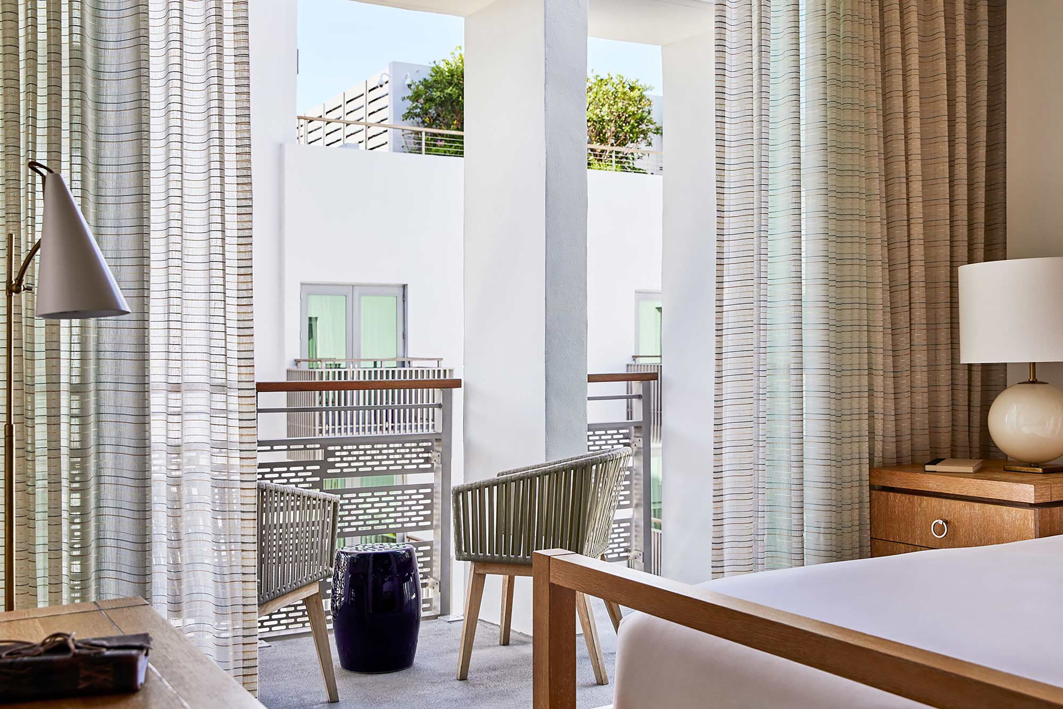 Una habitación de hotel con cama, escritorio, silla, lámpara y vista al exterior.