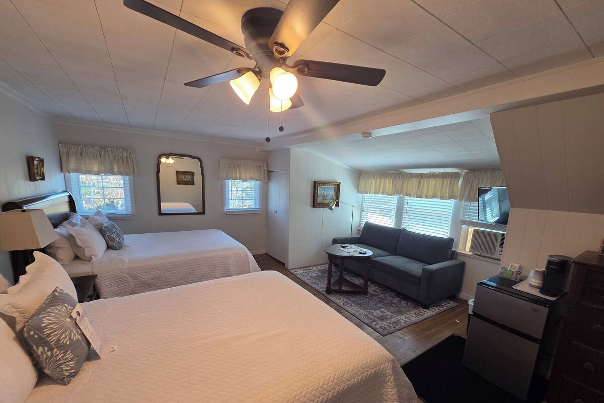 A hotel room with two beds, a ceiling fan, a small sofa, a coffee maker, and a refrigerator.