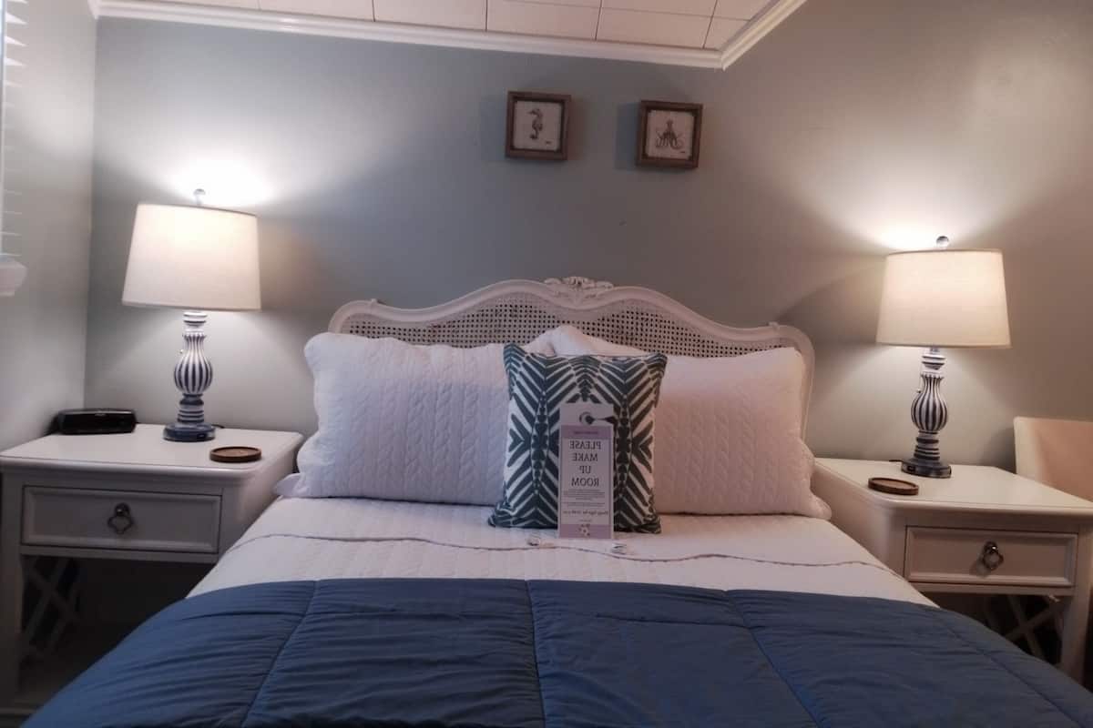A neatly arranged bedroom with a bed, two bedside tables, two lamps, and two framed pictures on the wall.
