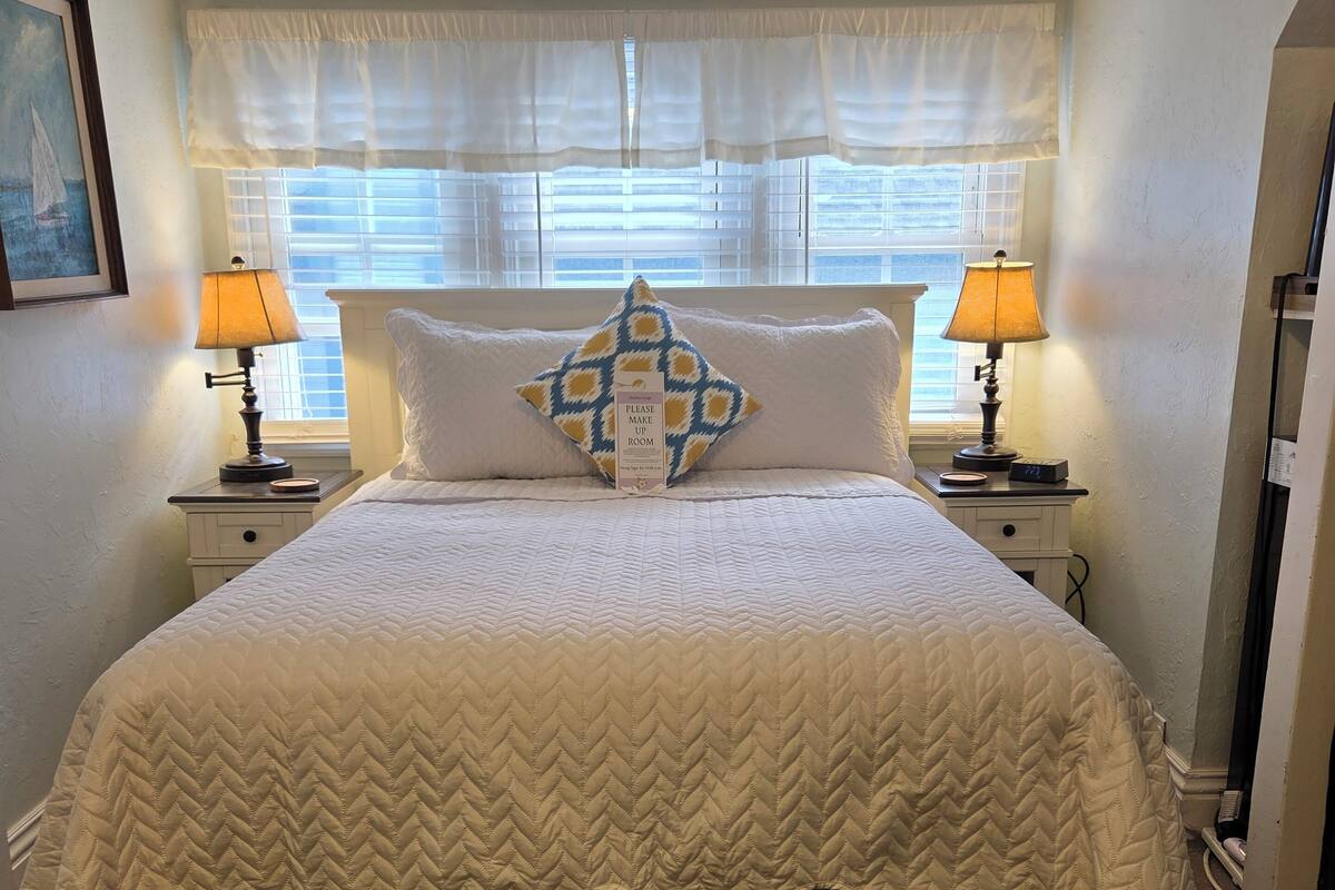 A neatly made bed with a quilted headboard, two bedside lamps, and a decorative pillow.