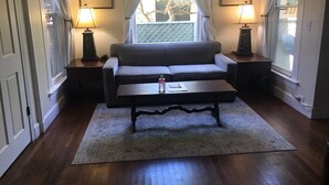 Un salon avec un canapé gris, une petite table basse, deux lampes et une fenêtre avec des rideaux.