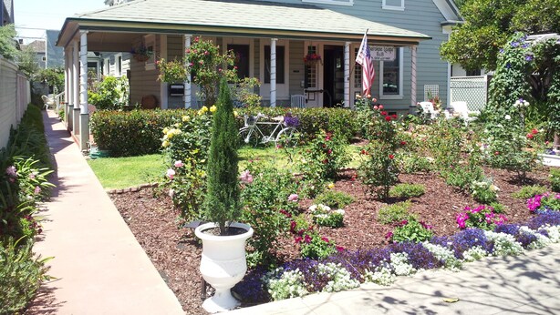 Une maison à deux étages avec un porche couvert, un jardin où poussent différentes sortes de fleurs et un drapeau américain.