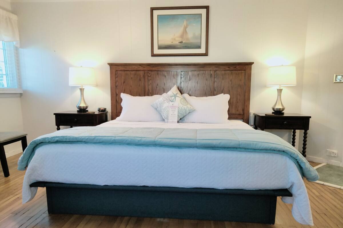 A neatly made bed with a wooden headboard, two bedside tables with lamps, and a framed picture above the headboard.