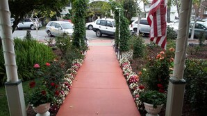 Un chemin bordé de plantes et de fleurs en pot, menant à l’entrée d’un bâtiment.