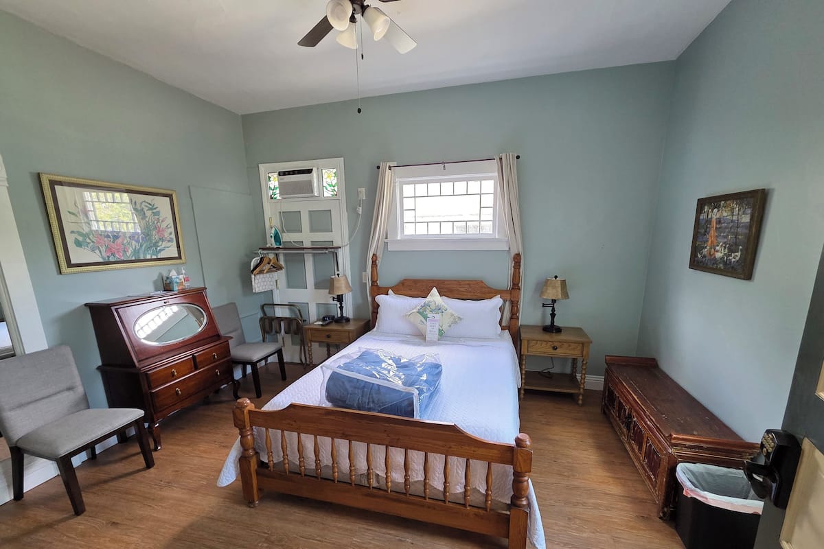 A bedroom with a wooden bed, a chair, a dresser, a vanity, and a ceiling fan.