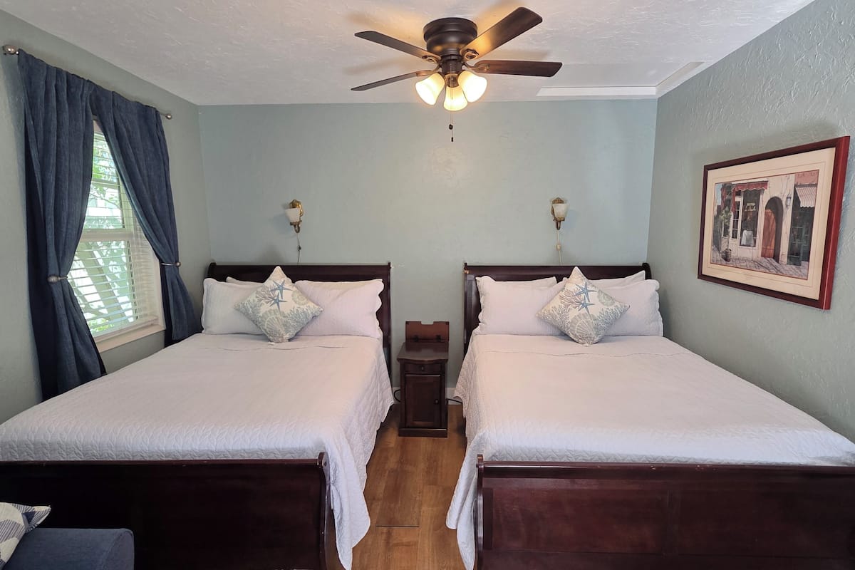 A room with two wooden beds, a ceiling fan, and a framed picture on the wall.