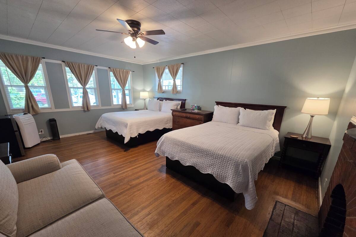 A hotel room with two beds, a ceiling fan, a nightstand with a lamp, a dresser, and a window with curtains.