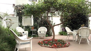 Un espace patio aménagé avec des meubles en osier blanc, un petit arbre et un parterre de fleurs.