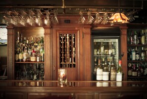 A bar area with shelves of liquor bottles, a wine cooler, and hanging wine glasses. - Belfry Inn & Bistro (Sandwich)
