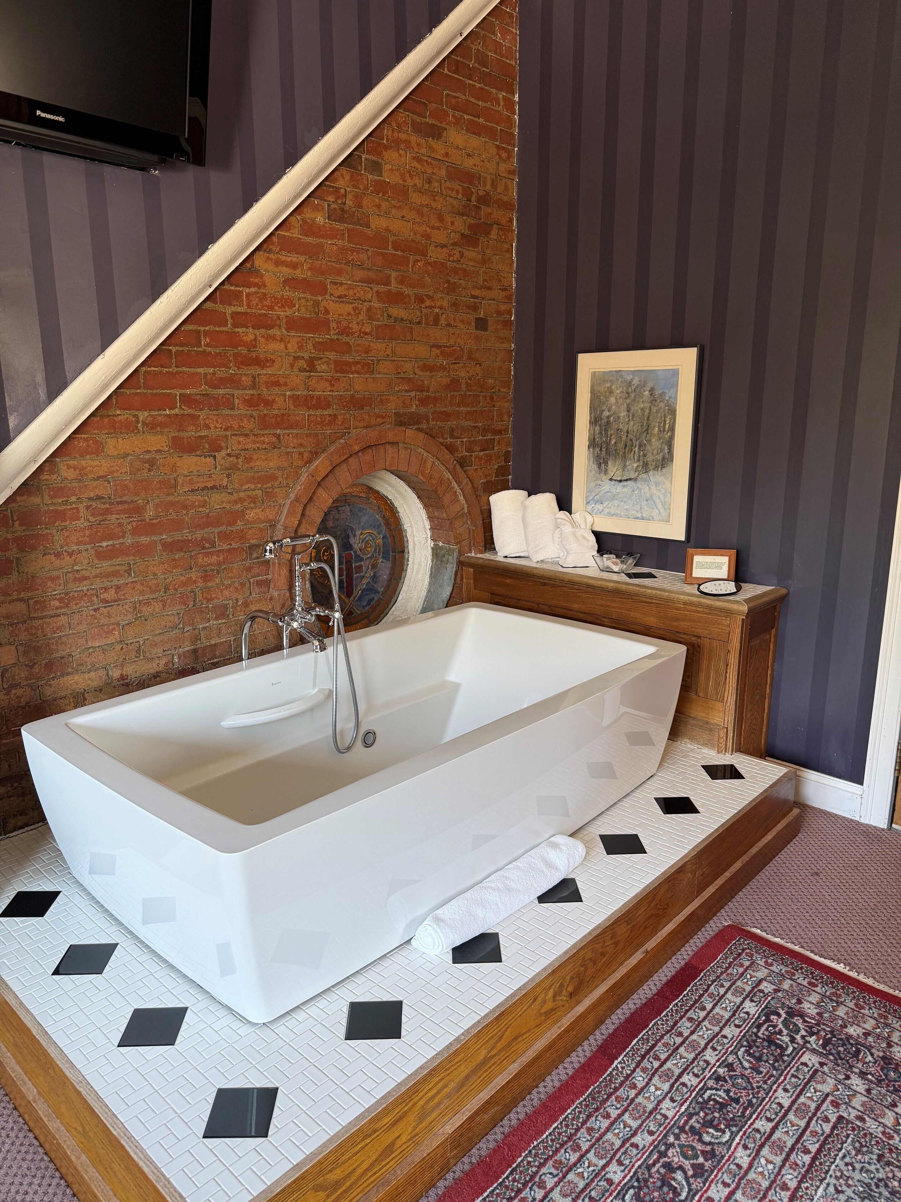 A modern bathroom with a freestanding bathtub, a wooden vanity, and a brick wall.