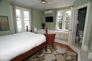 Quarto com cama, uma cadeira vermelha, banheira e janela com vista para o exterior.
