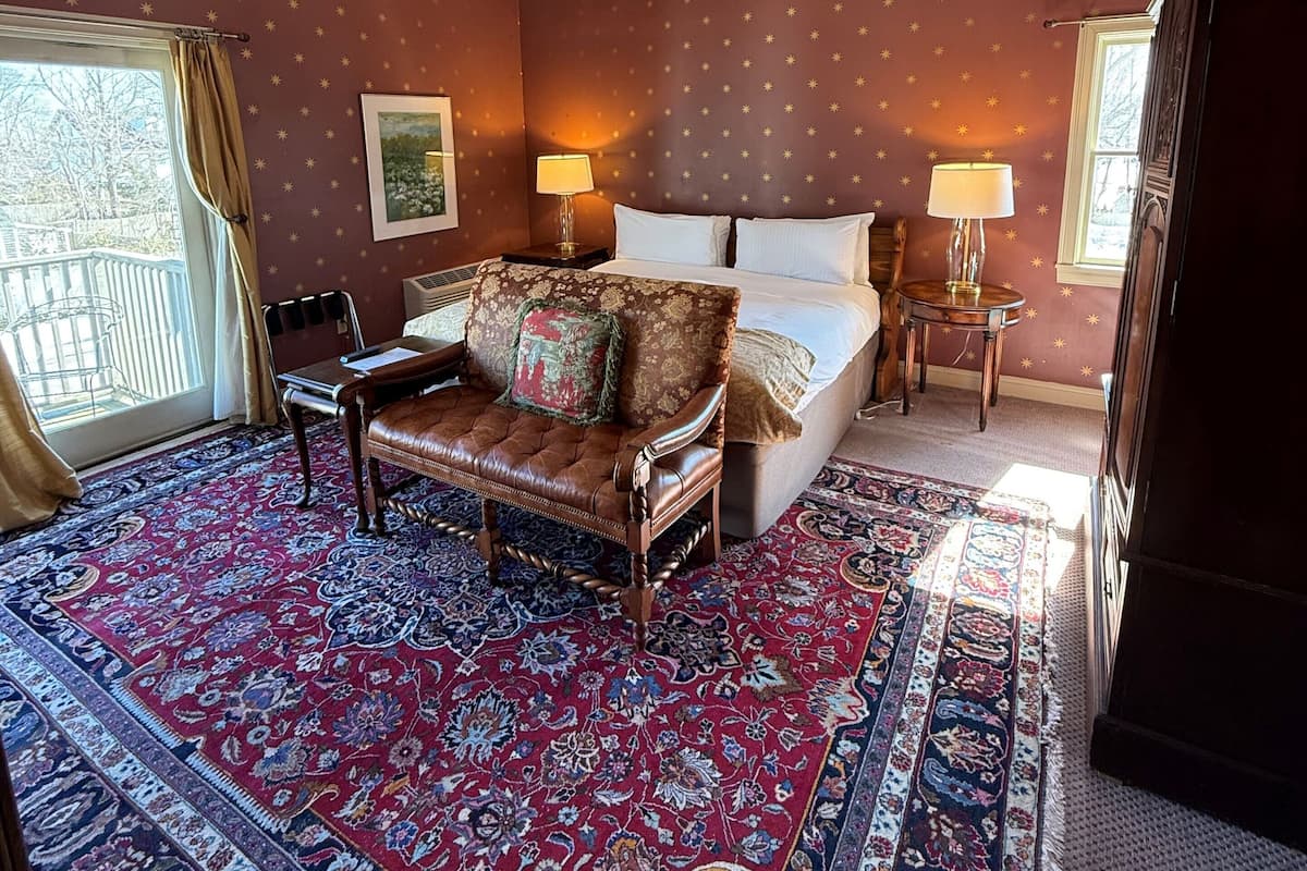A bedroom with a large bed, a sofa, a ceiling fan, and a patterned rug.