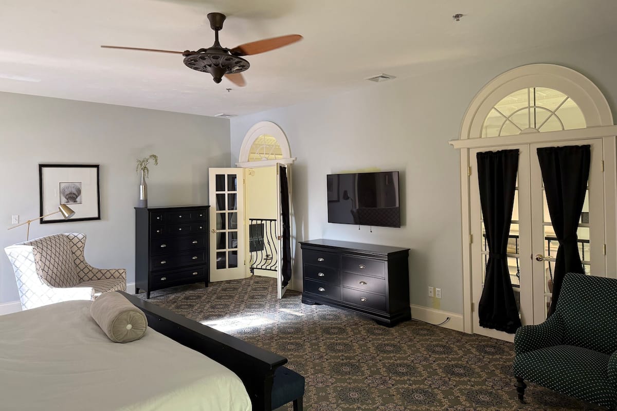 A bedroom with a bed, a dresser, a TV, a ceiling fan, and a window with curtains.