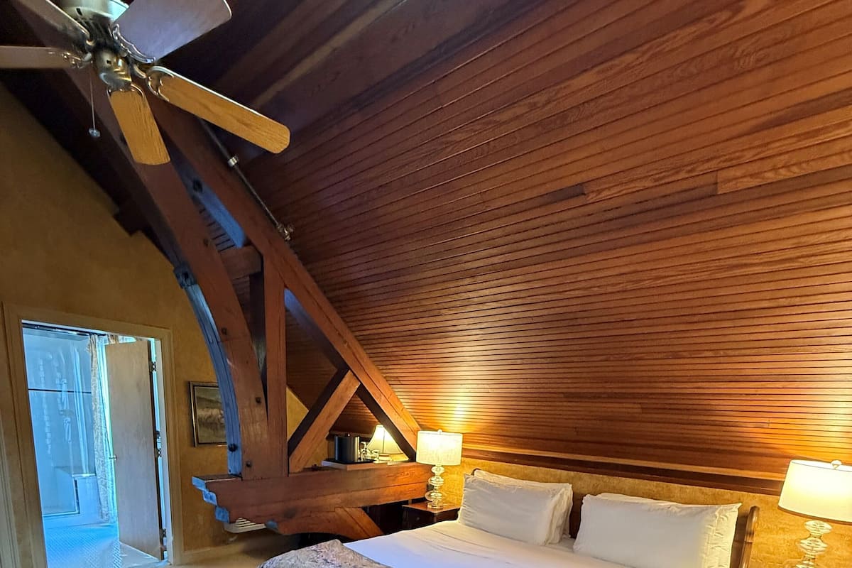 A bedroom with a large bed, wooden ceiling beams, and a ceiling fan.