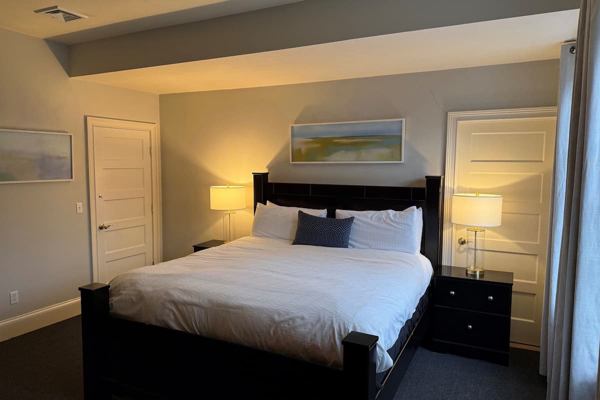 A hotel room with a bed, two bedside tables, a painting on the wall, and a door.
