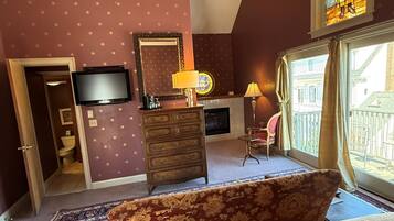 A bedroom with a bed, a dresser, a television, a ceiling fan, a stained glass window, and a view of the outside.