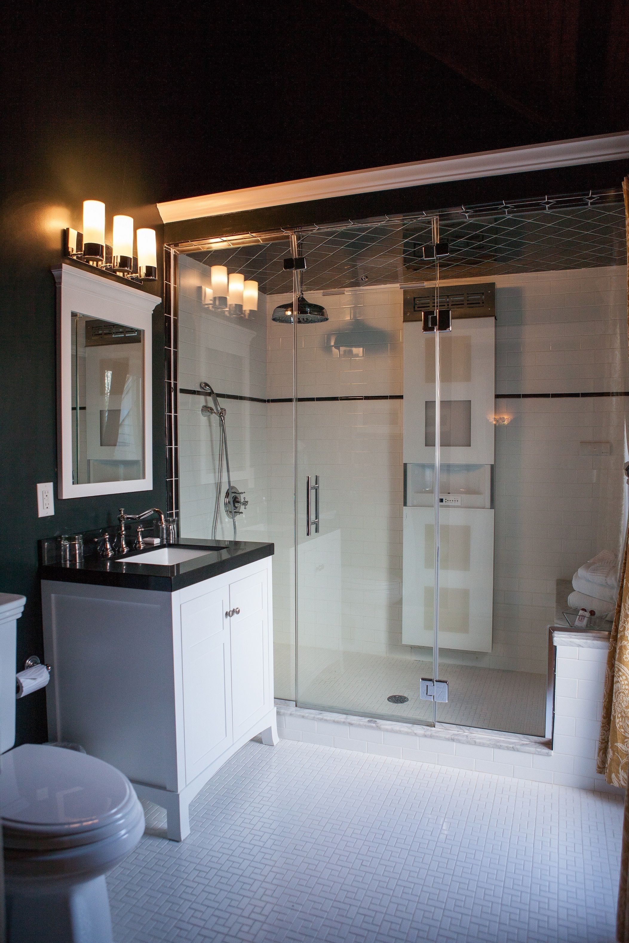 A modern bathroom with a glass-enclosed shower, white cabinetry, and a large mirror above the sink.