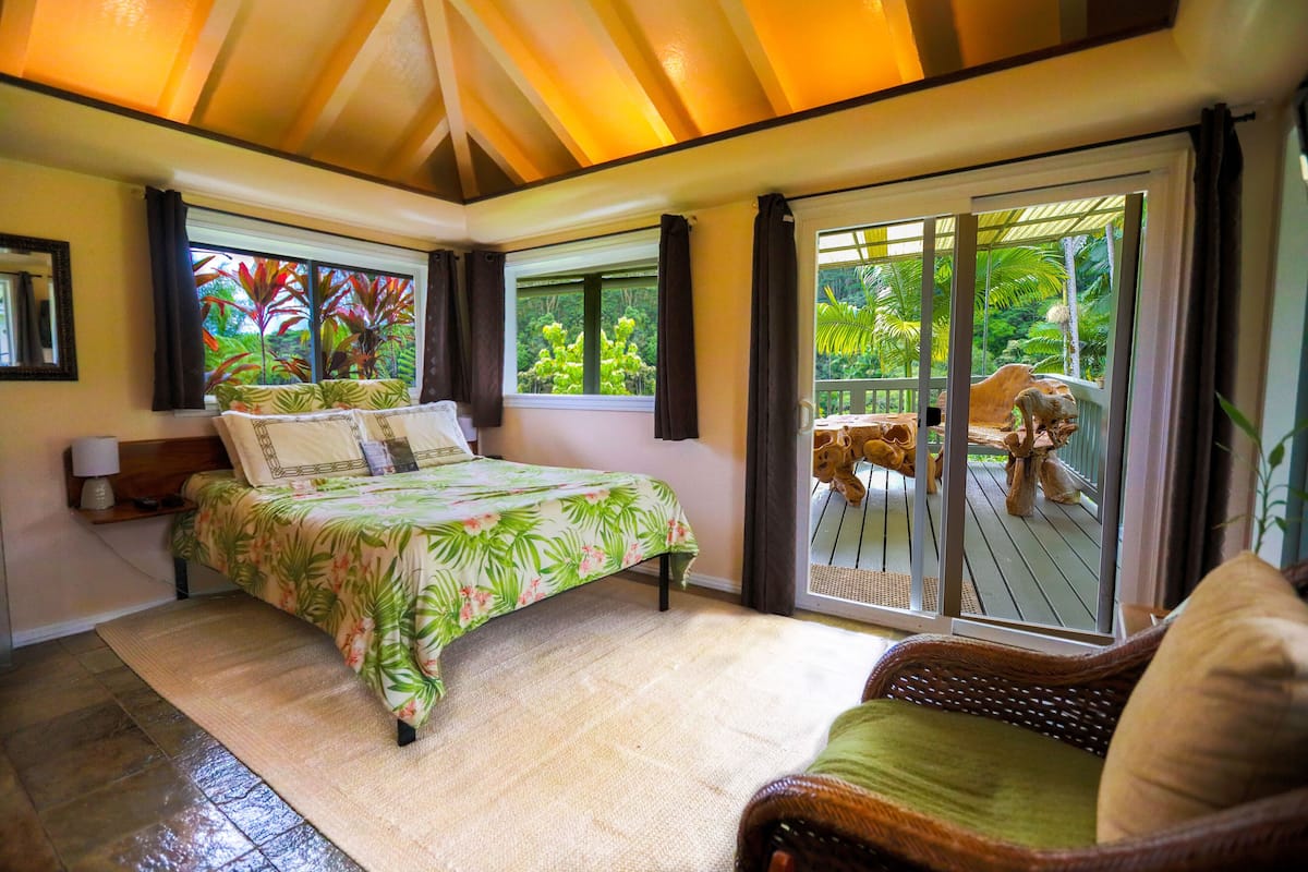 Un dormitorio con cama, mesita de noche, ventana con cortinas y vistas al exterior.