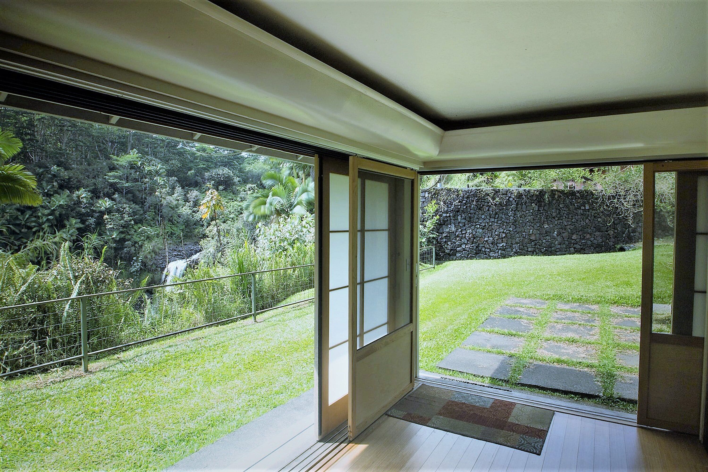 A room with a sliding glass door leading to a garden with a stone wall and a grassy lawn.