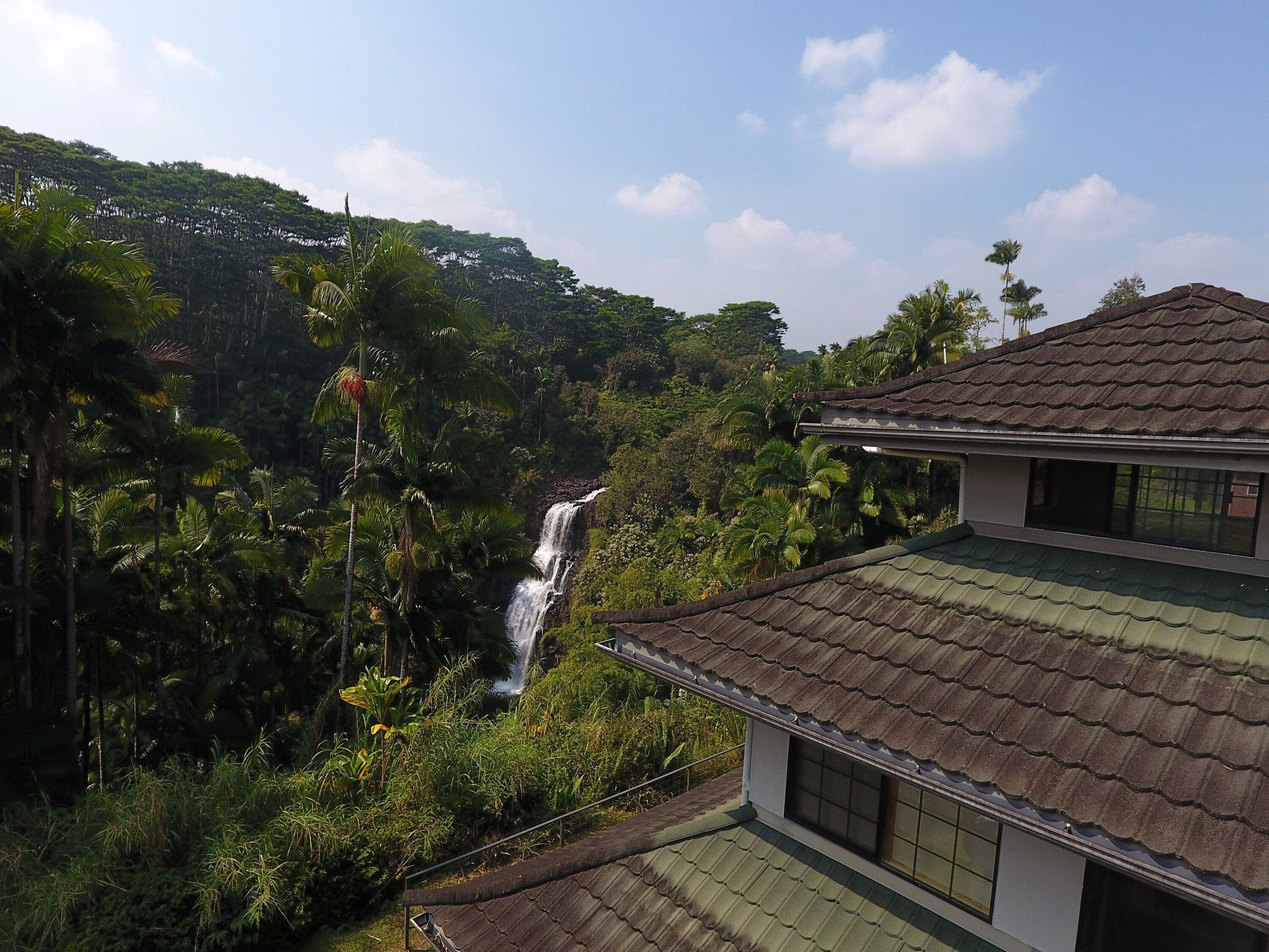 A house with a tiled roof overlooking a waterfall and dense greenery.
