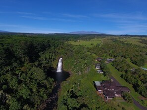 Vista aérea de un paisaje exuberante con una cascada, vegetación densa y algunas edificaciones residenciales.