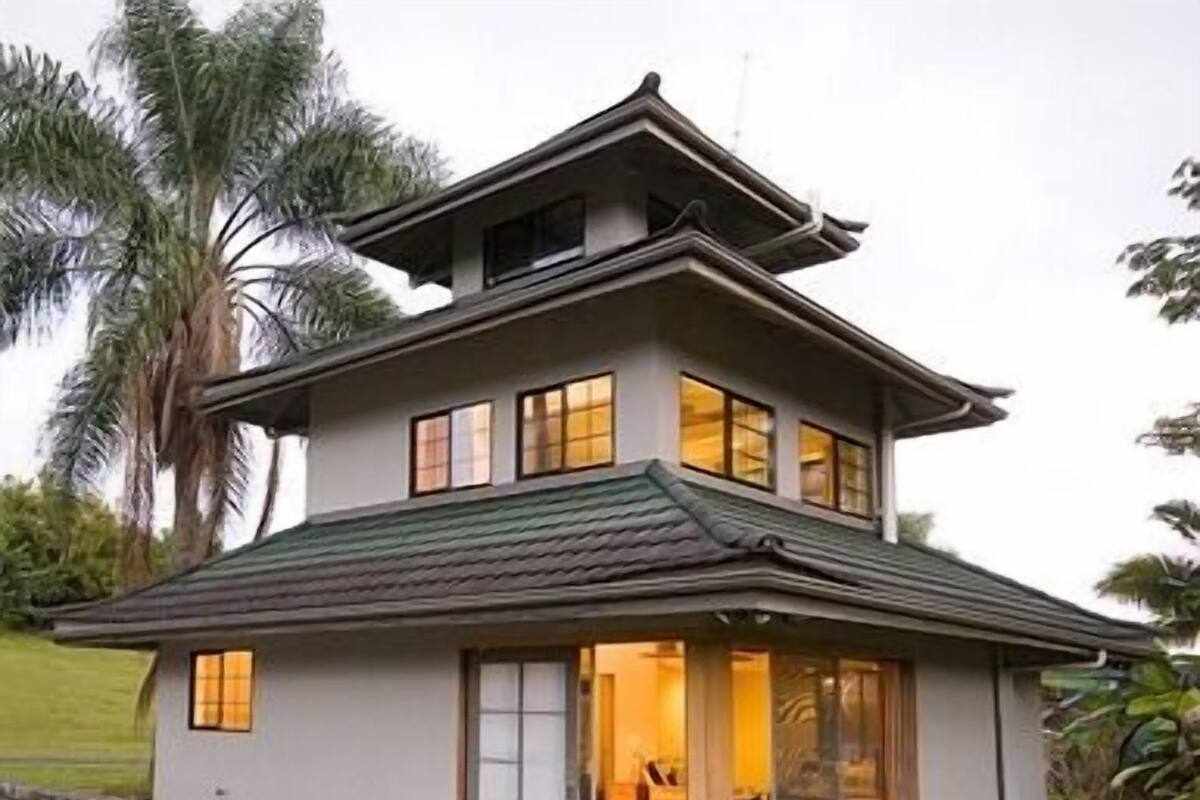 Una casa de dos pisos con techo inclinado, ventanas grandes y cimientos de piedra.