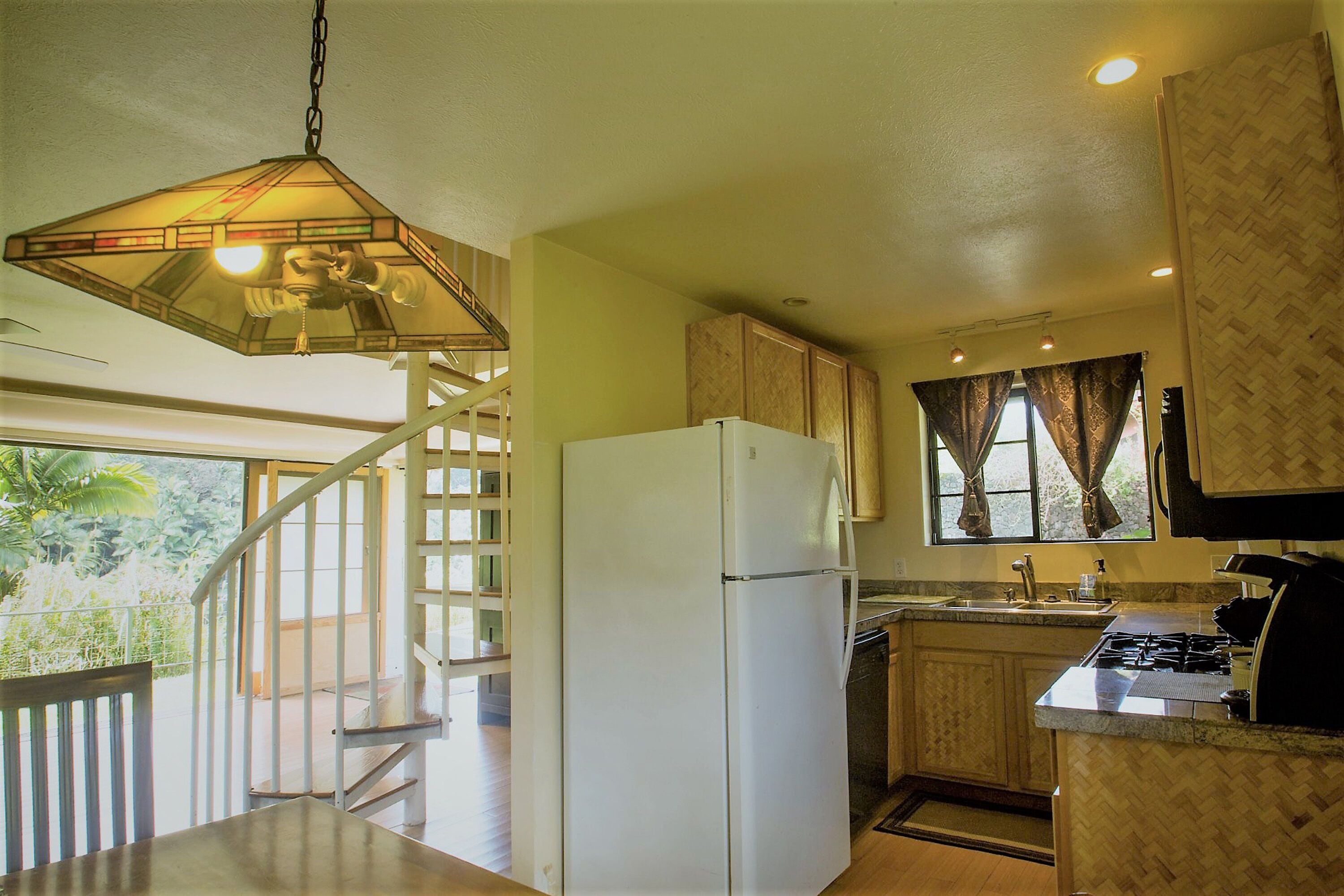 A kitchen with a white refrigerator, a stove, and a hanging light fixture.