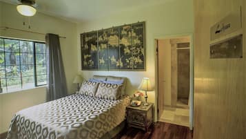 A bedroom with a bed, a nightstand, a wall-mounted artwork, a window with curtains, and a door with a sign.
