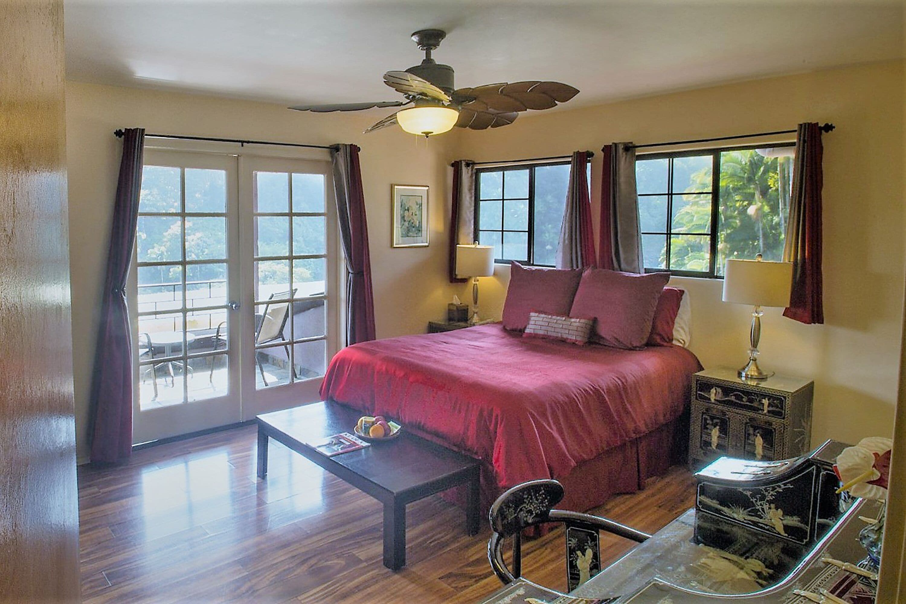 A bedroom with a bed, a desk, a chair, a ceiling fan, and a window with curtains.