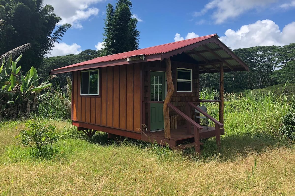 Una cabaña de madera pequeña con techo rojo, un porche y una puerta verde.