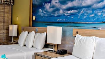 A hotel room with a bed, bedside tables, a lamp, and a large beach view painting on the wall.