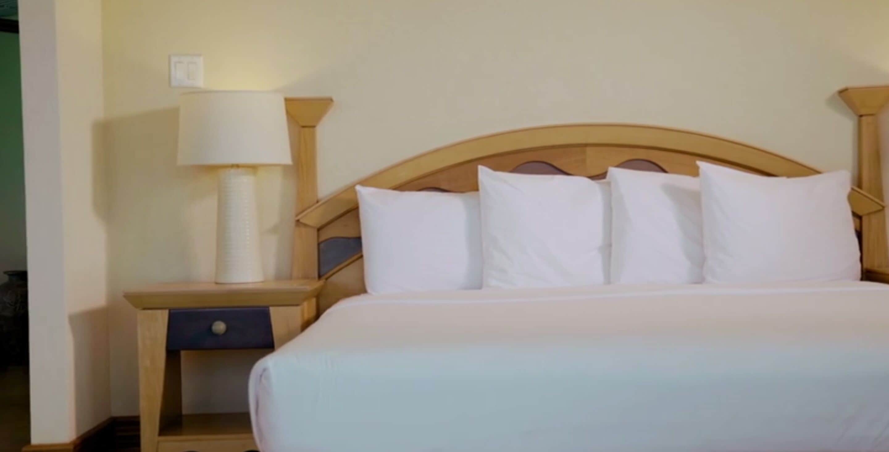 A neatly made bed with white linens and a wooden headboard.