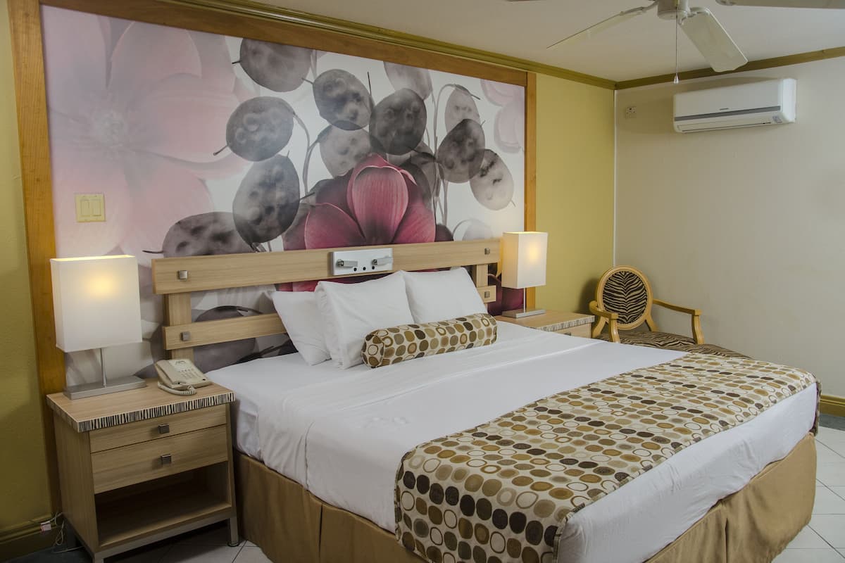 Ein Hotelzimmer mit Bett, Nachttischen, einer Lampe, einem Telefon, einem Sessel und einer Wand-Klimaanlage.
