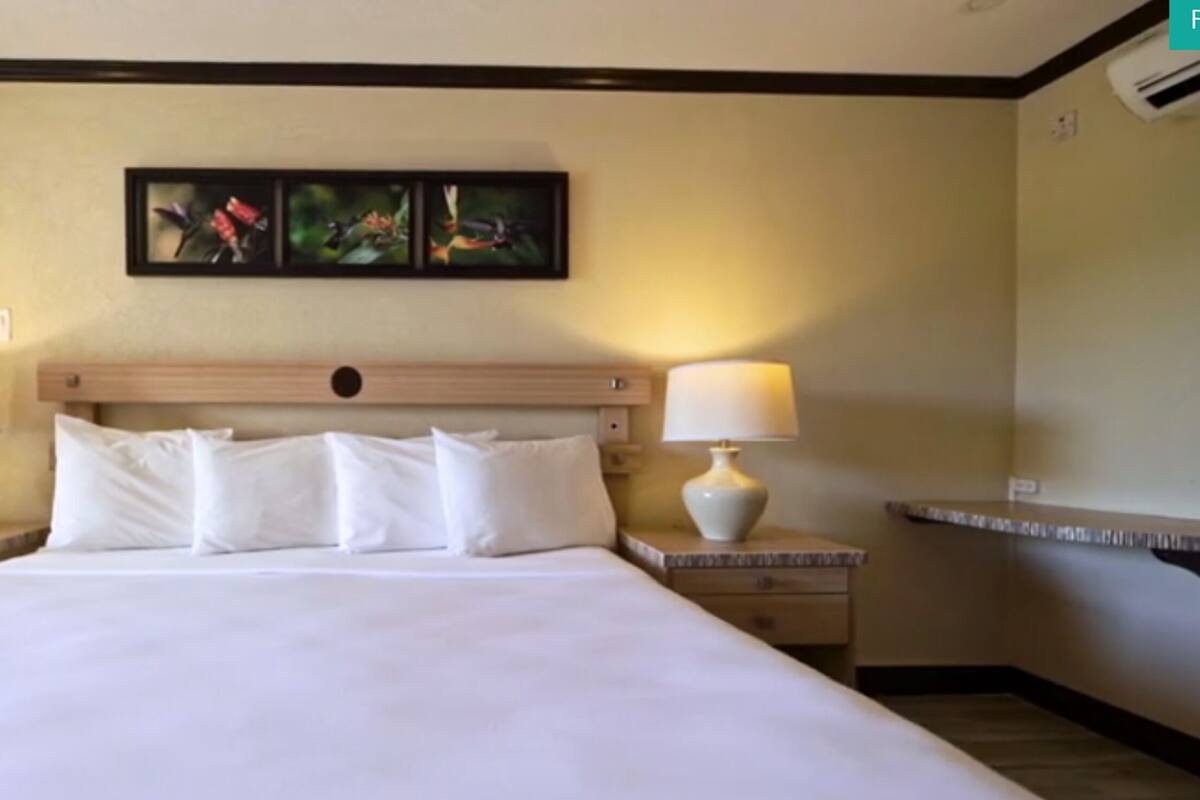 Ein Hotelzimmer mit einem großen Bett, zwei Nachttischen mit Lampen und einem an der Wand hängenden Kunstwerk darüber.
