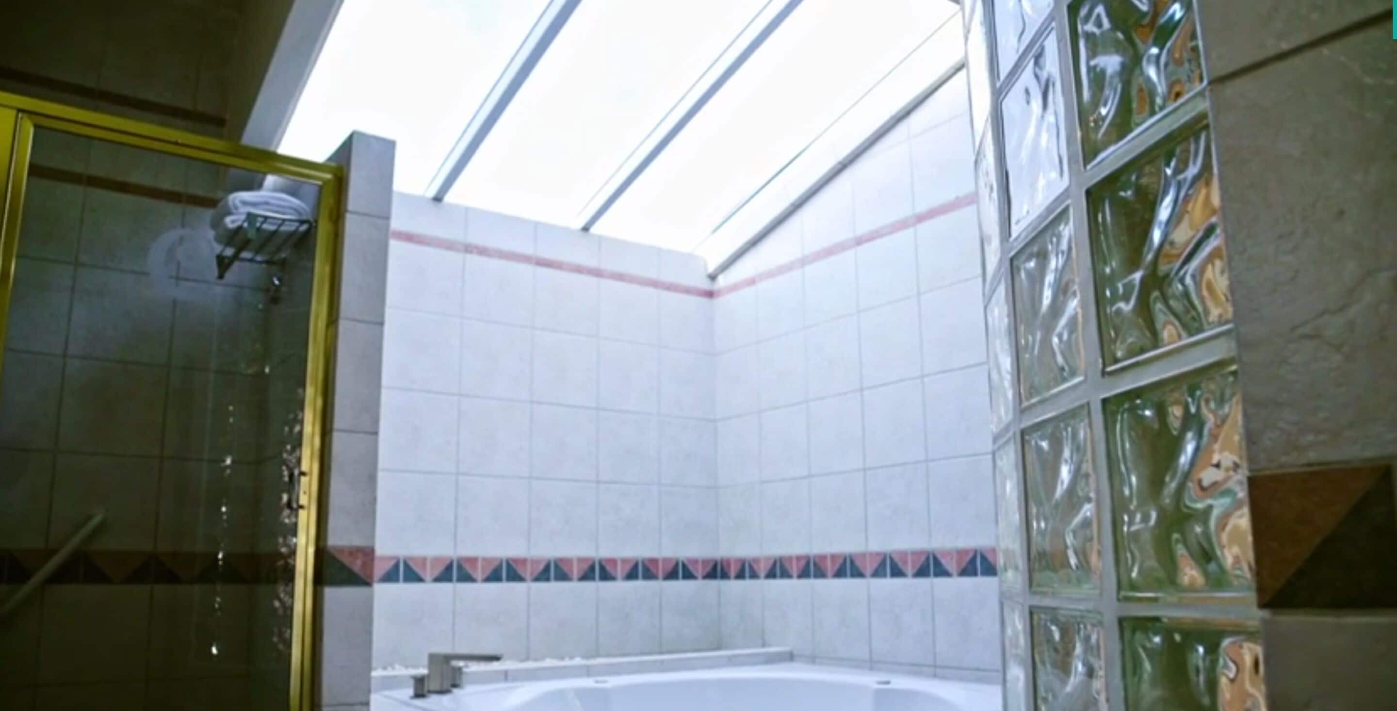 Un baño con cabina de ducha de vidrio, bañera y paredes de azulejos con un detalle decorativo.