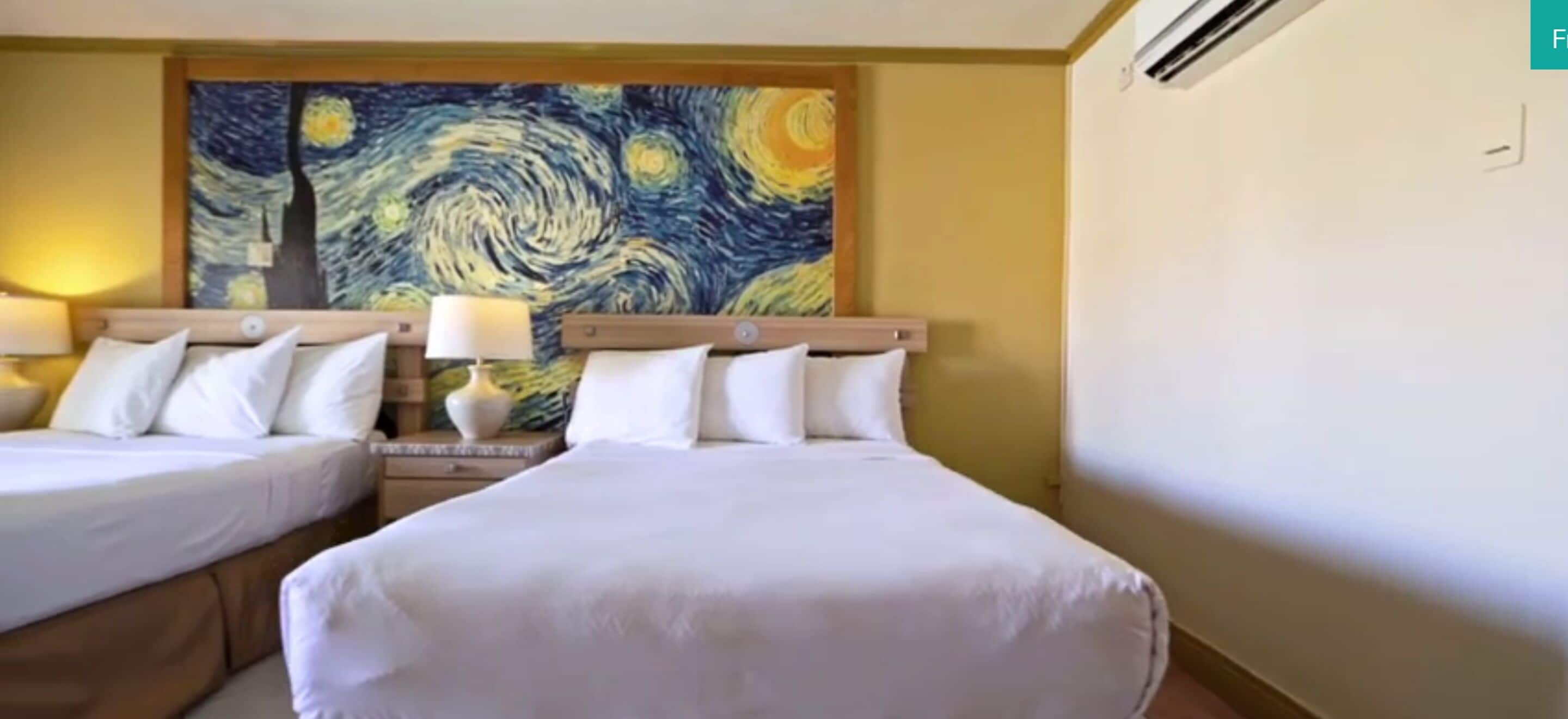 A hotel room with two beds, a large painting on the wall, and a nightstand with a lamp.